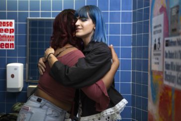 A non-binary femme embracing another student.